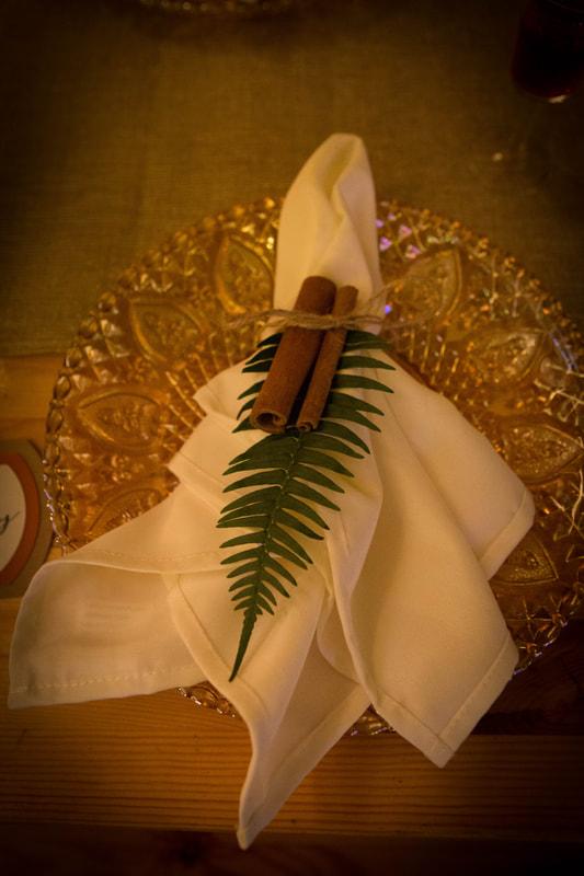 Gold charger plates with white napkin, cinnamon sticks and fern