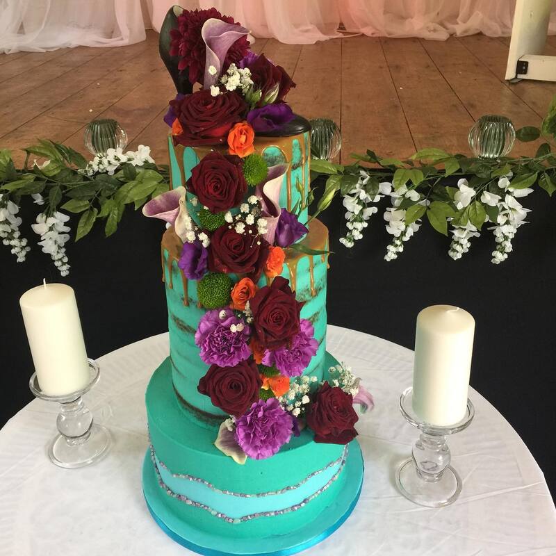 Blue semi naked wedding cake with fresh flower cascade down the front. 