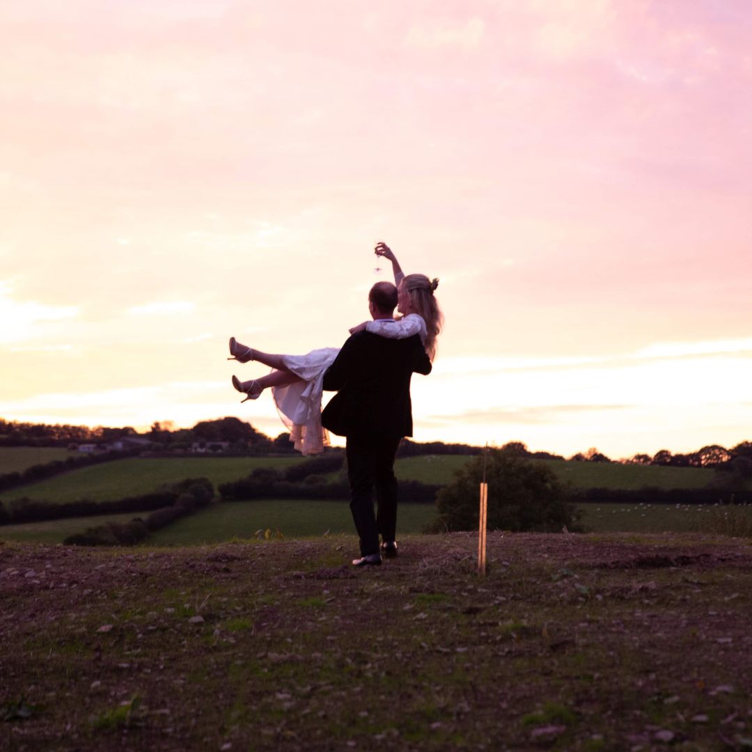 Groom holding bride with sunset in background