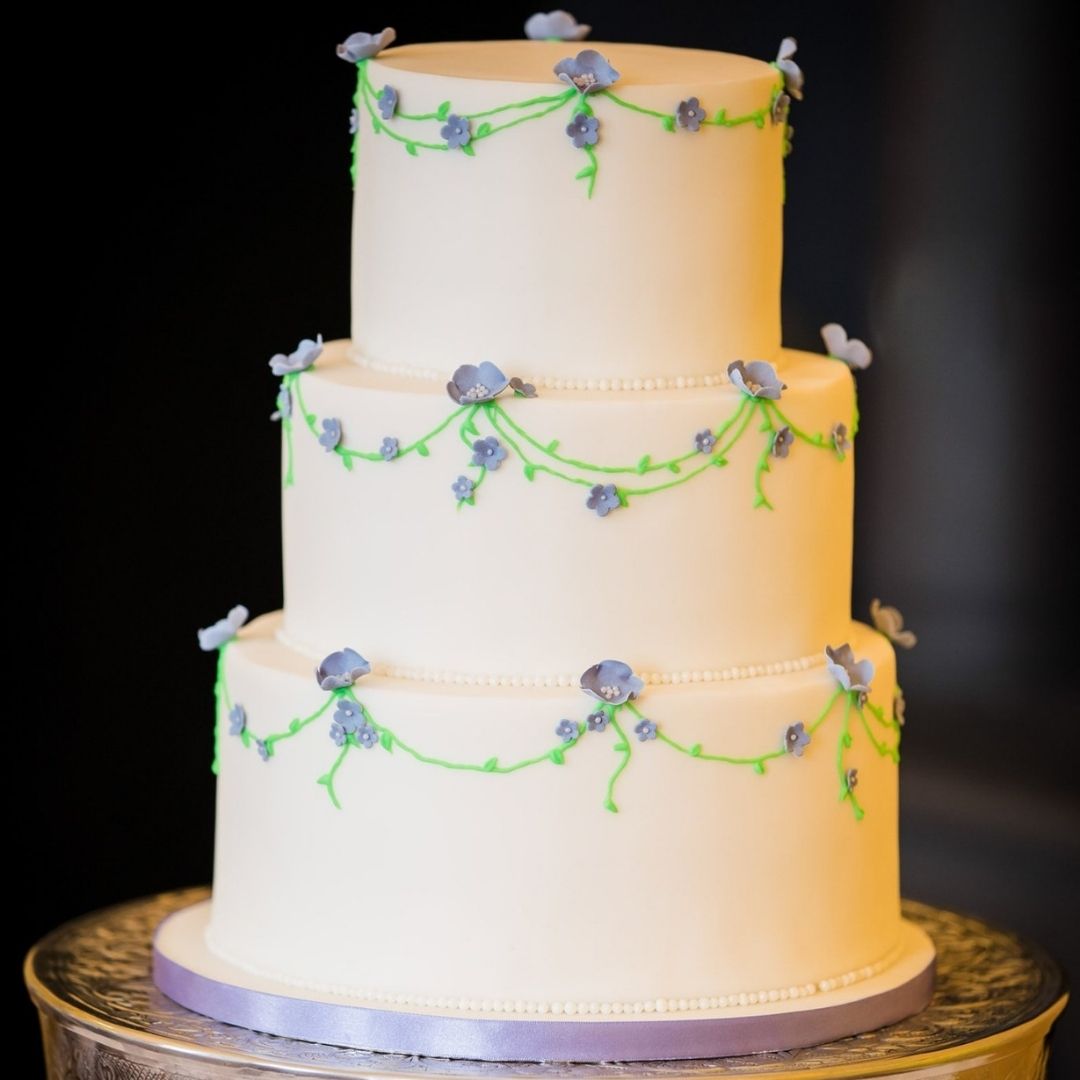 Three tier fondant wedding cake with small blue flowers and hand piped vines